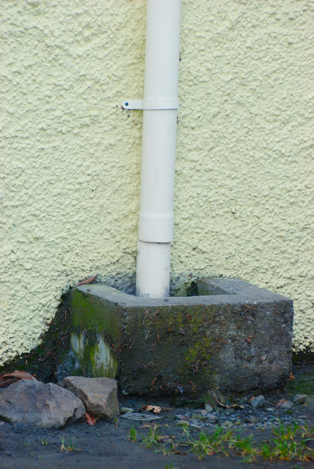 a white pipe sticking out of the ground next to a wall