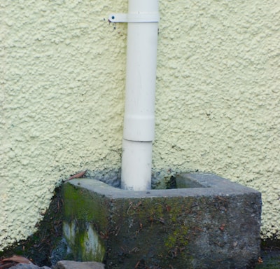 a white pipe sticking out of the ground next to a wall