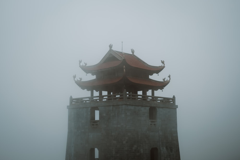 a tall tower with a red roof on a foggy day