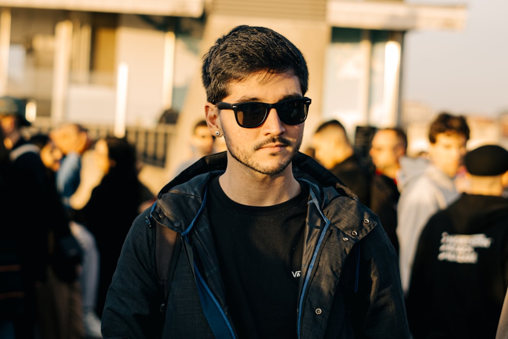 a man wearing sunglasses standing in front of a crowd of people