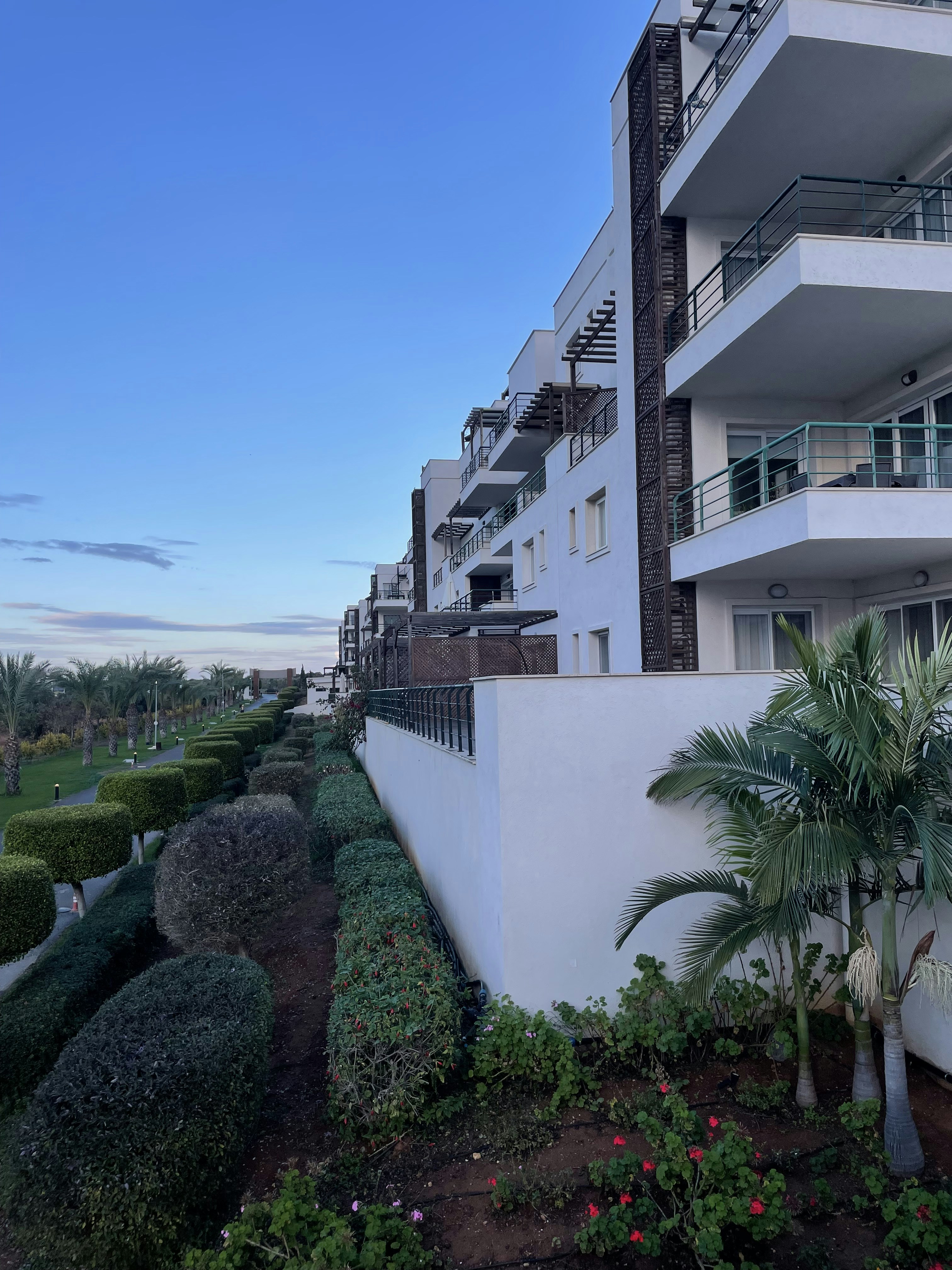 Modern white condo building with balconies, palm trees, bright California sunshine, clean architecture