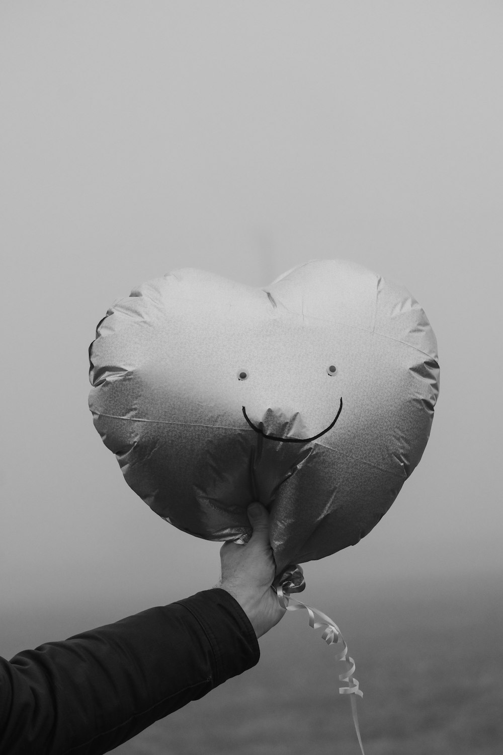 a black and white photo of a person holding a heart shaped balloon