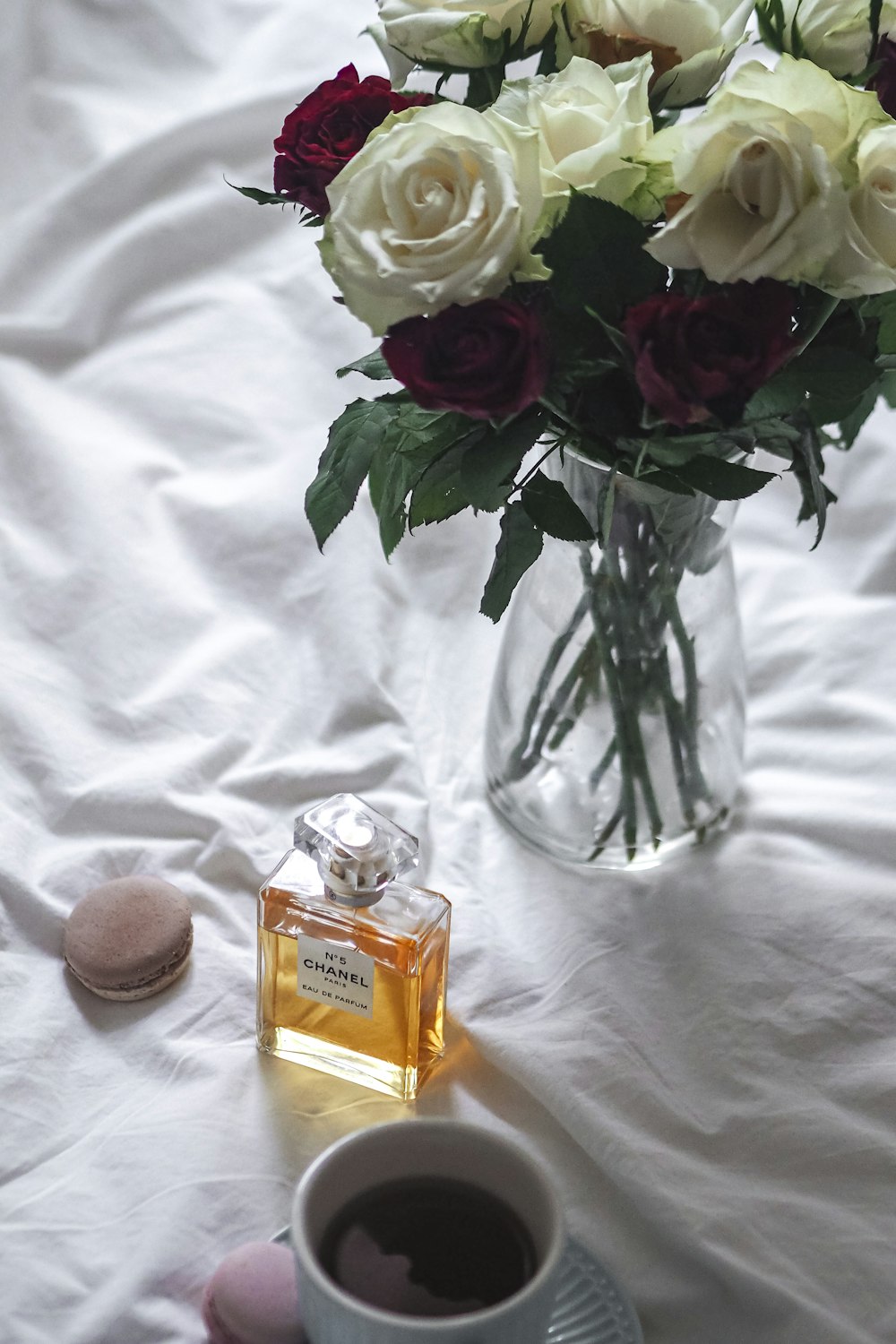 a glass vase filled with white roses next to a cup of coffee