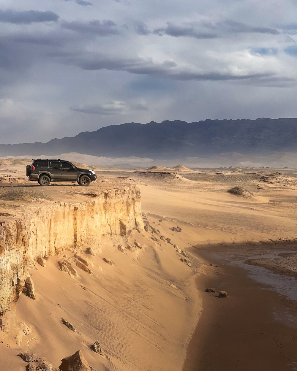 a jeep driving on a desert road near a cliff