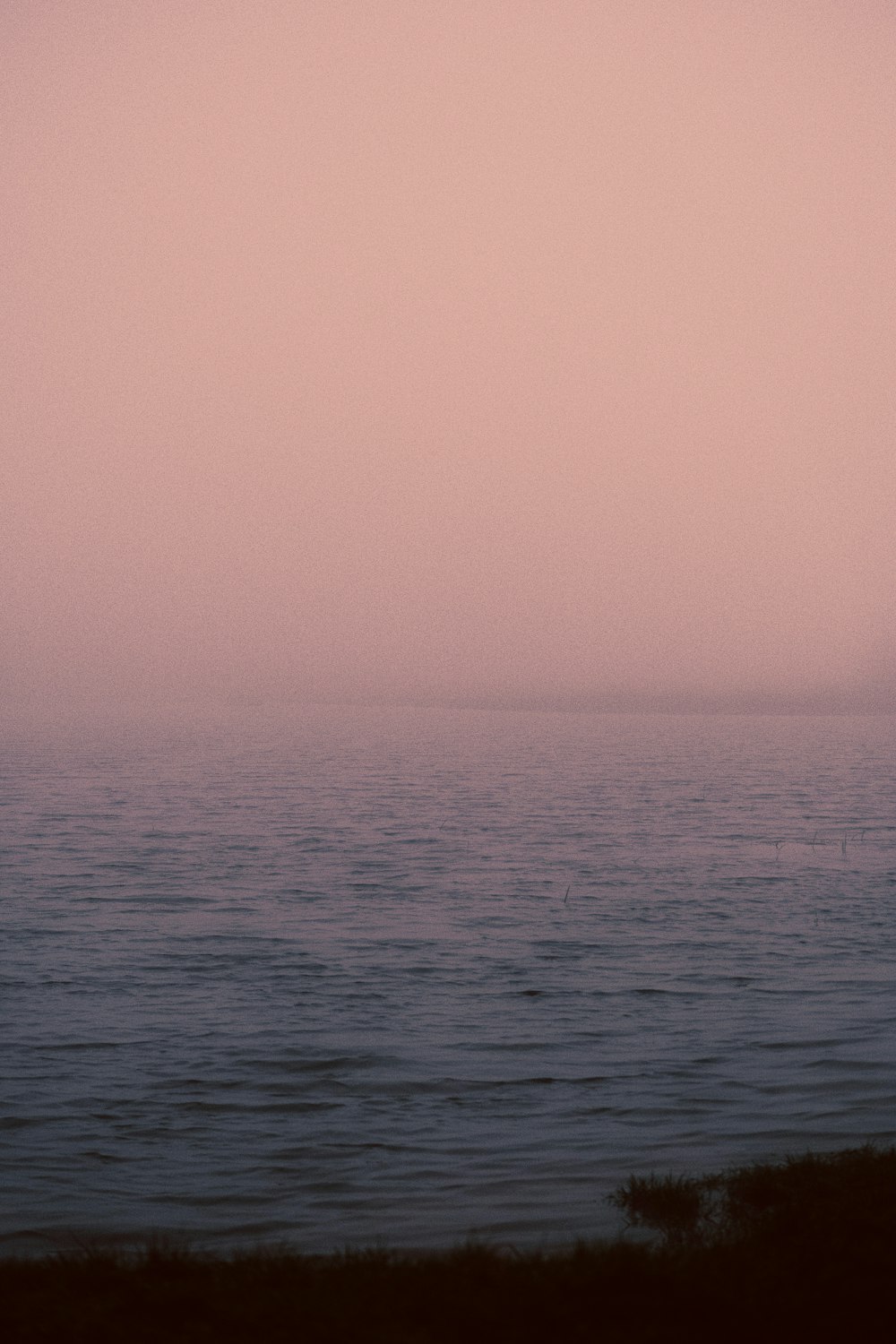 a large body of water sitting under a pink sky