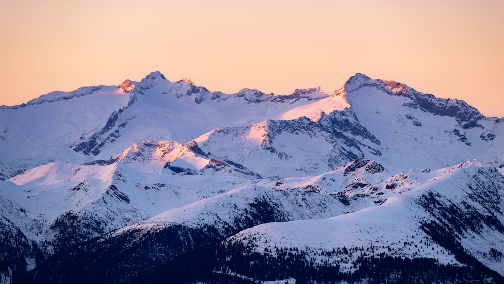 a mountain range covered in snow at sunset