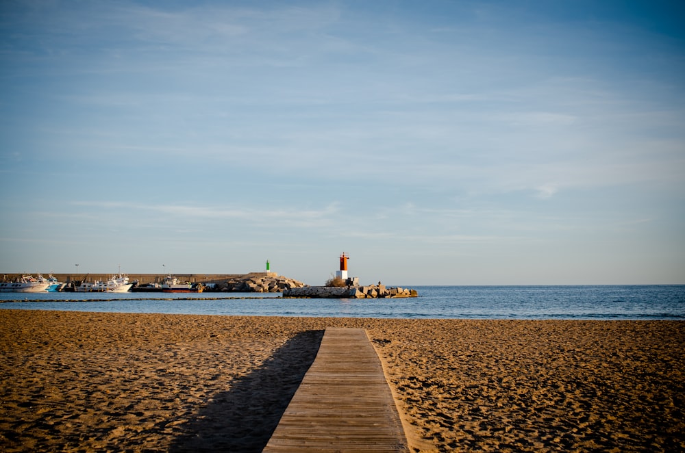a wooden walkway leading to a beach with a lighthouse in the background