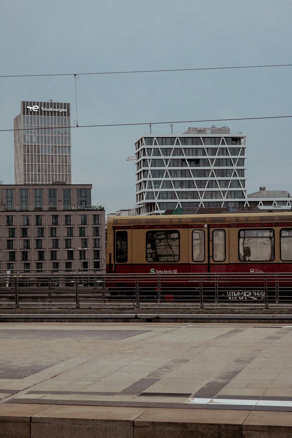 a red and yellow train traveling past tall buildings