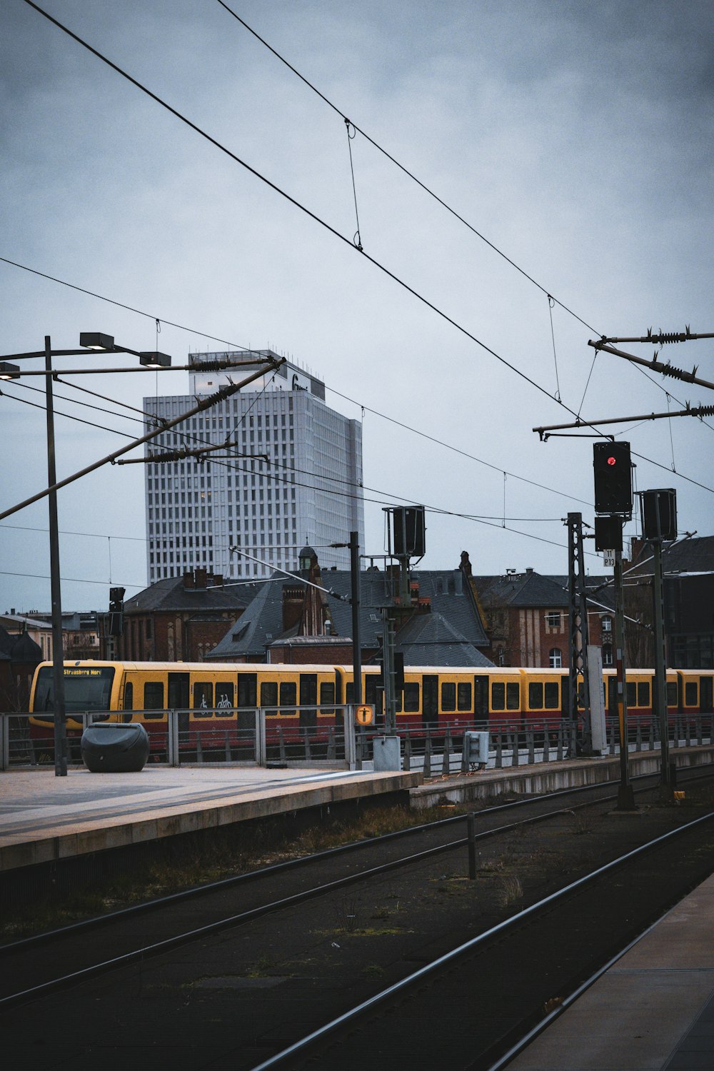 Ein gelber Zug, der neben einem hohen Gebäude auf Bahngleisen fährt