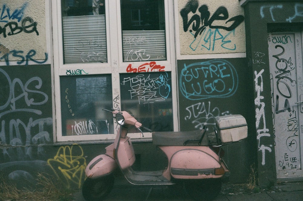 a pink scooter parked in front of a building covered in graffiti