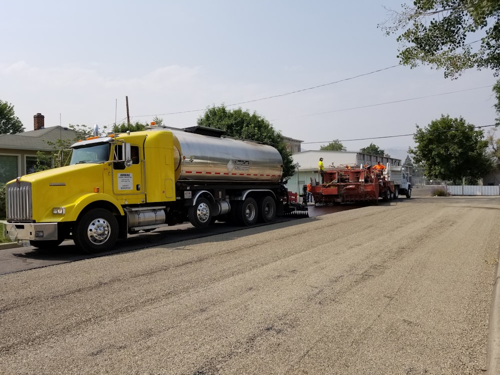 a yellow tanker truck pulling a red trailer down a street