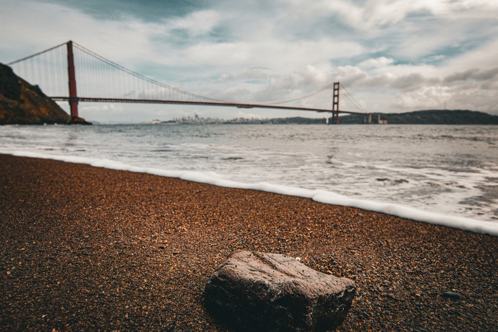 a rock on a beach with a bridge in the background