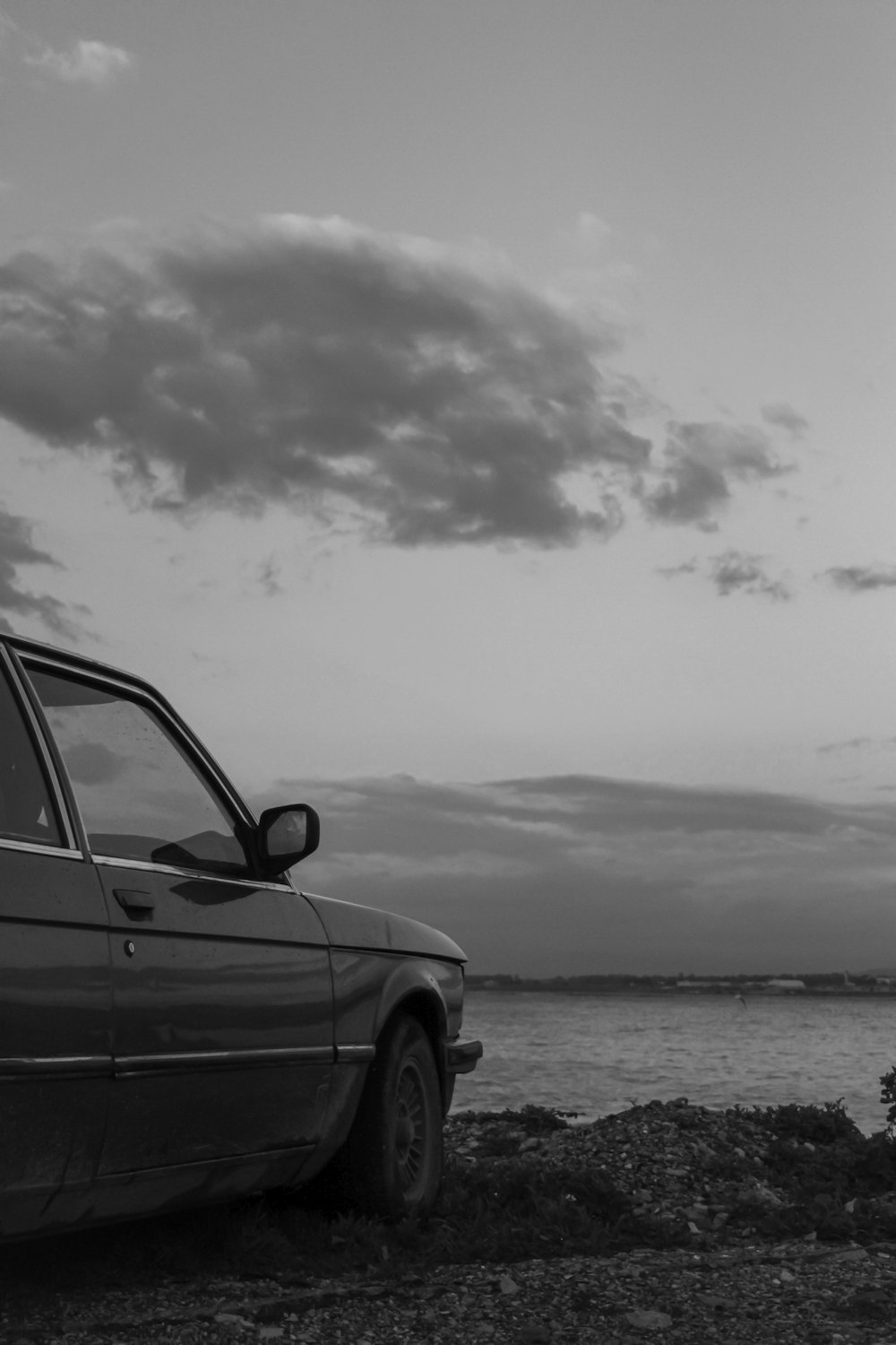 a black and white photo of a car by the water