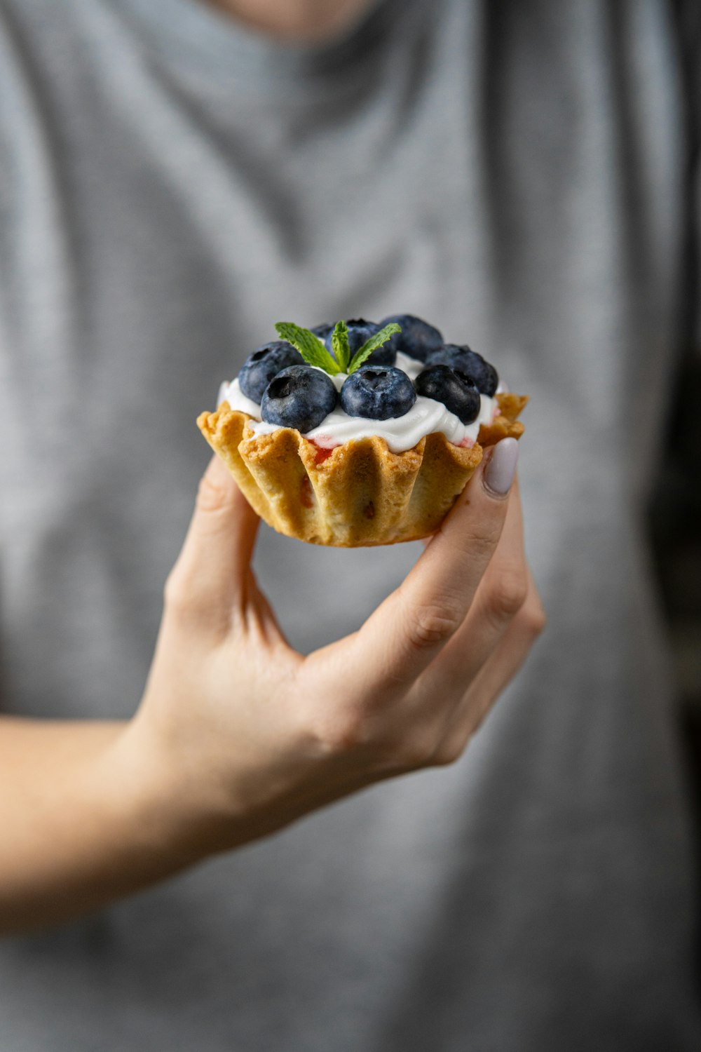 a person holding a pastry with blueberries and cream