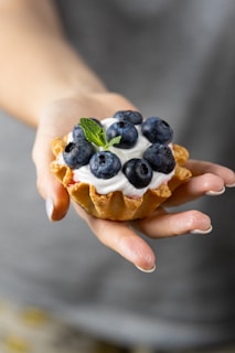 a person holding a pastry with blueberries and whipped cream
