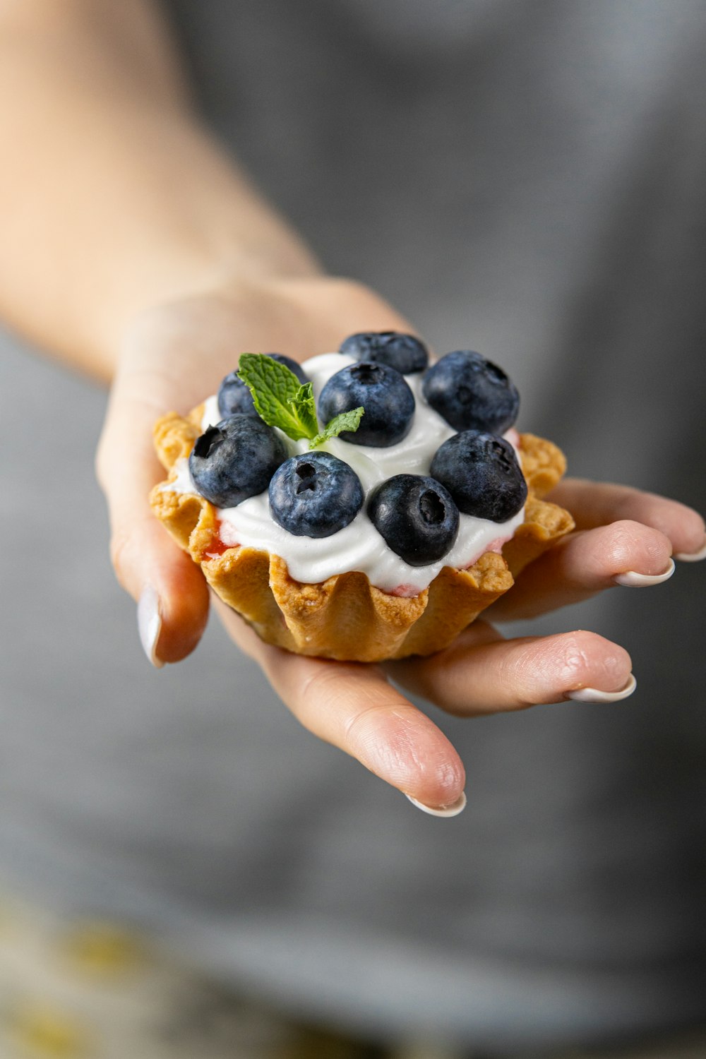a person holding a pastry with blueberries and whipped cream