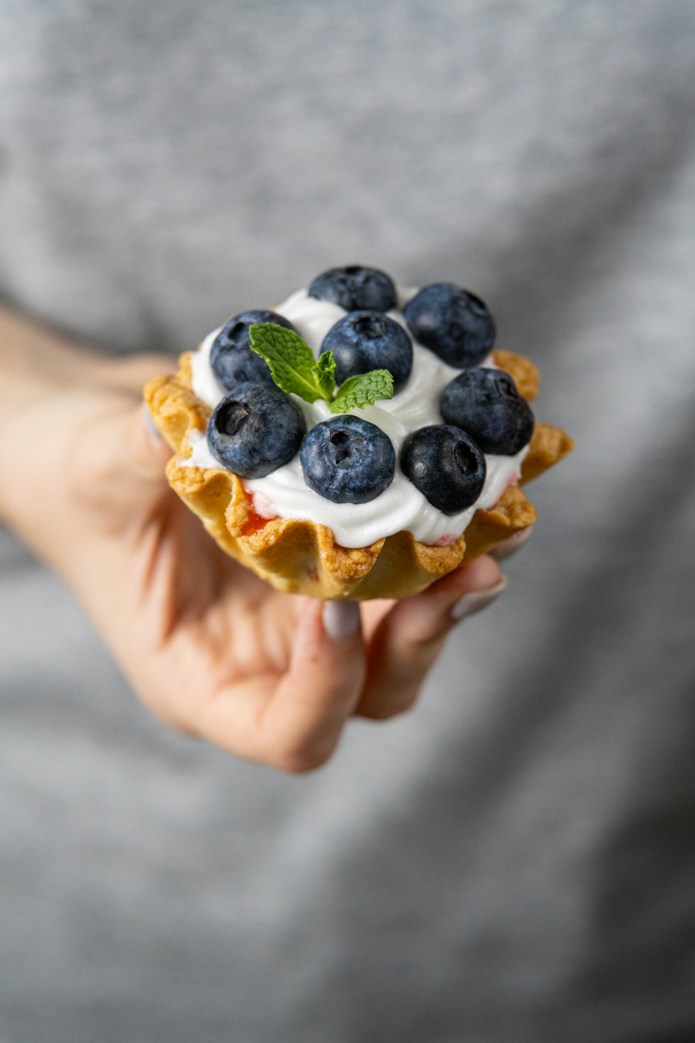 a person holding a pastry with blueberries and whipped cream