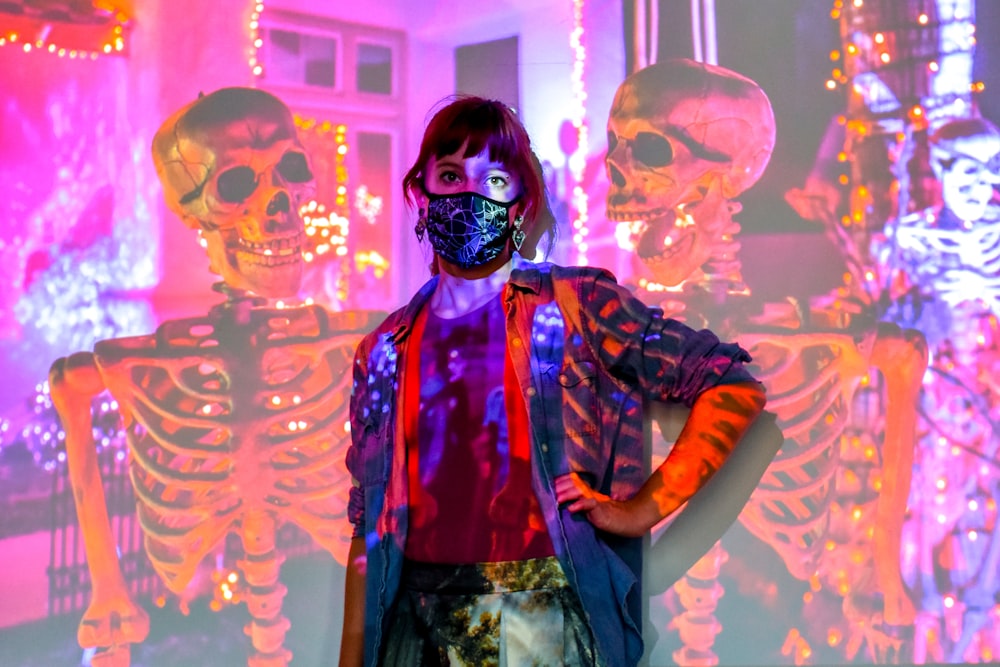 a woman in a skeleton mask standing in front of a wall of skeletons