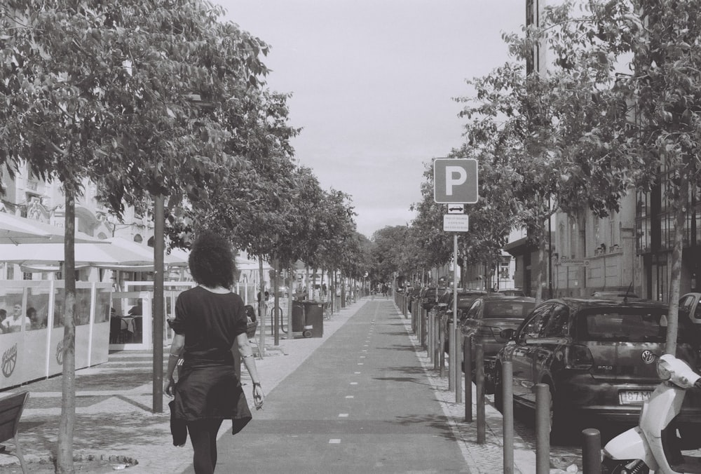 a woman walking down a street next to parked cars