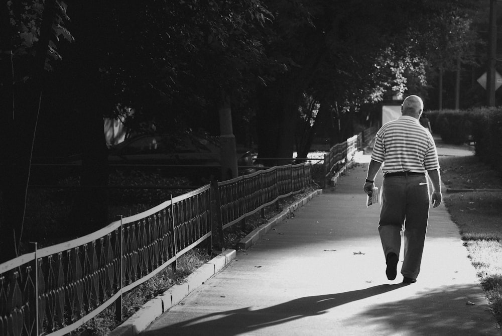 a man walking down a sidewalk holding a skateboard