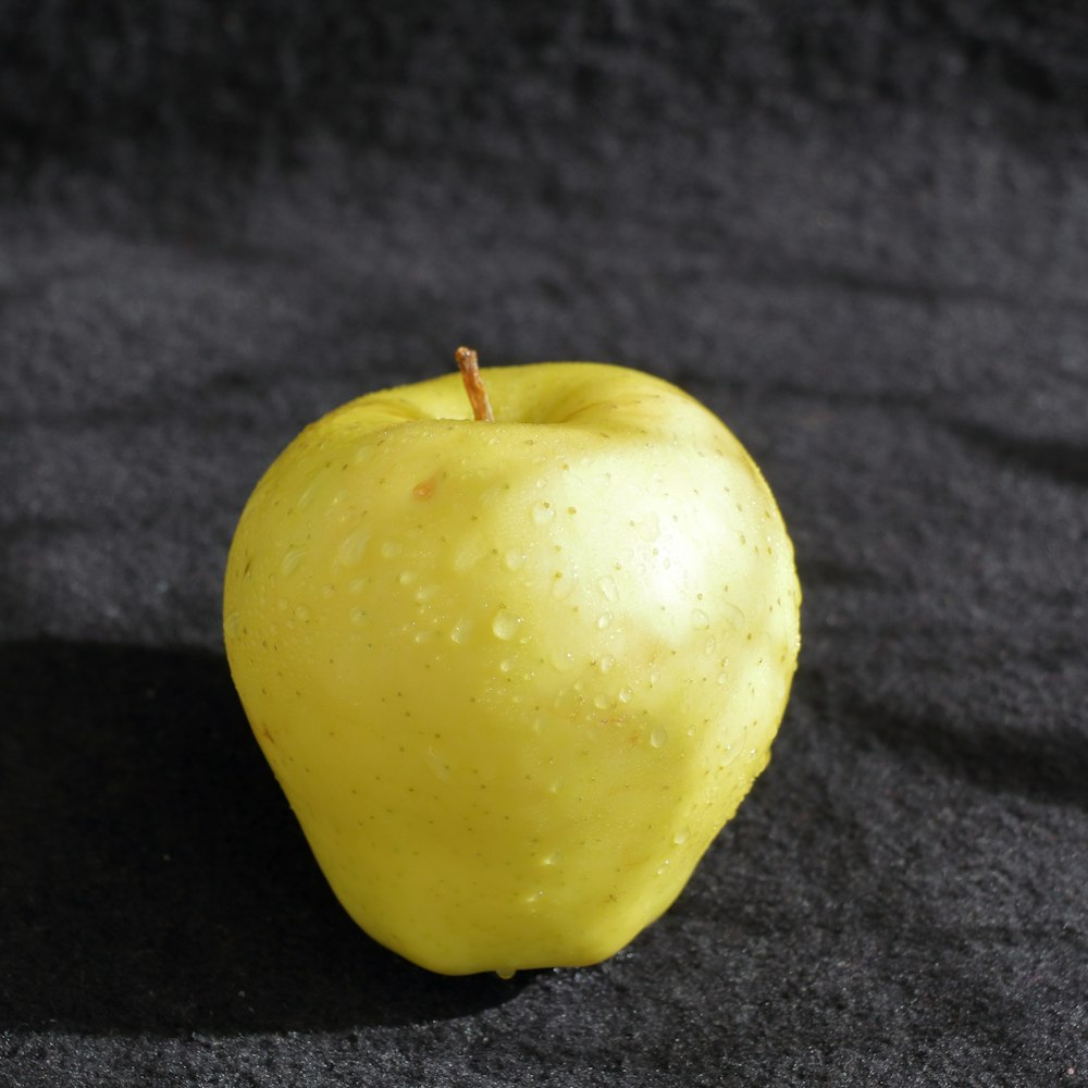 a yellow apple sitting on top of a black surface