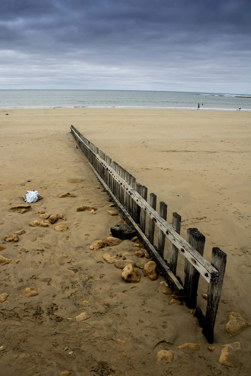 a broken fence on a beach with a body of water in the background
