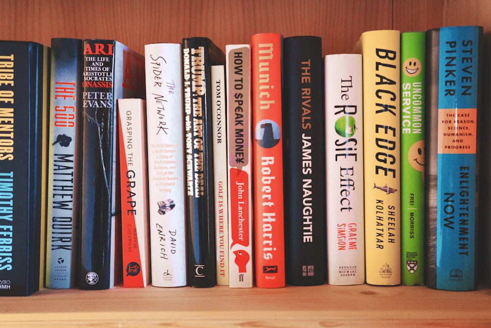 a row of books sitting on top of a wooden shelf