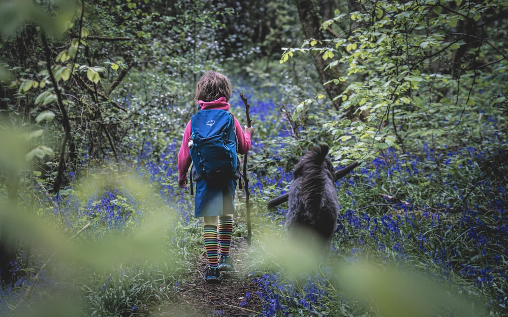 a little girl walking through a forest with a dog