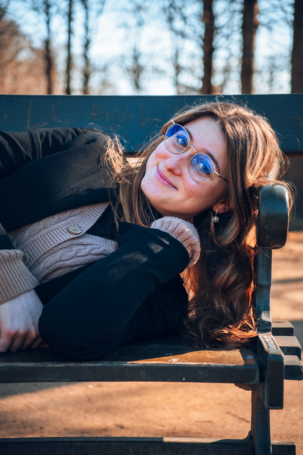 a woman wearing glasses laying on a bench