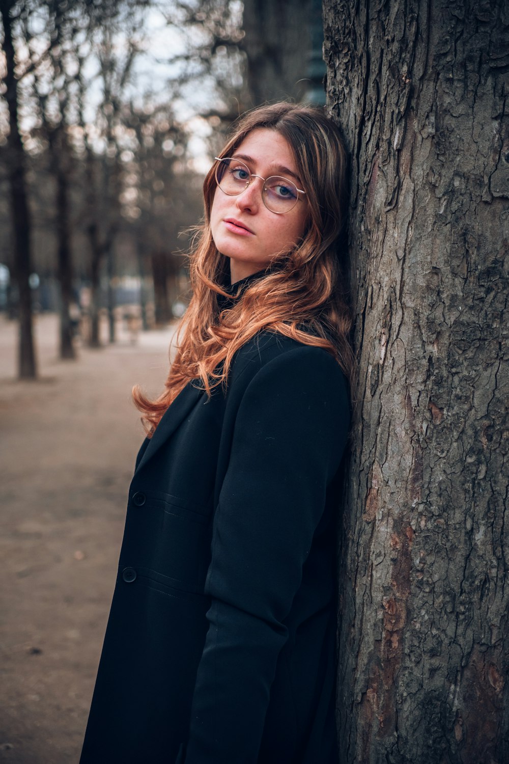 a woman wearing glasses leaning against a tree