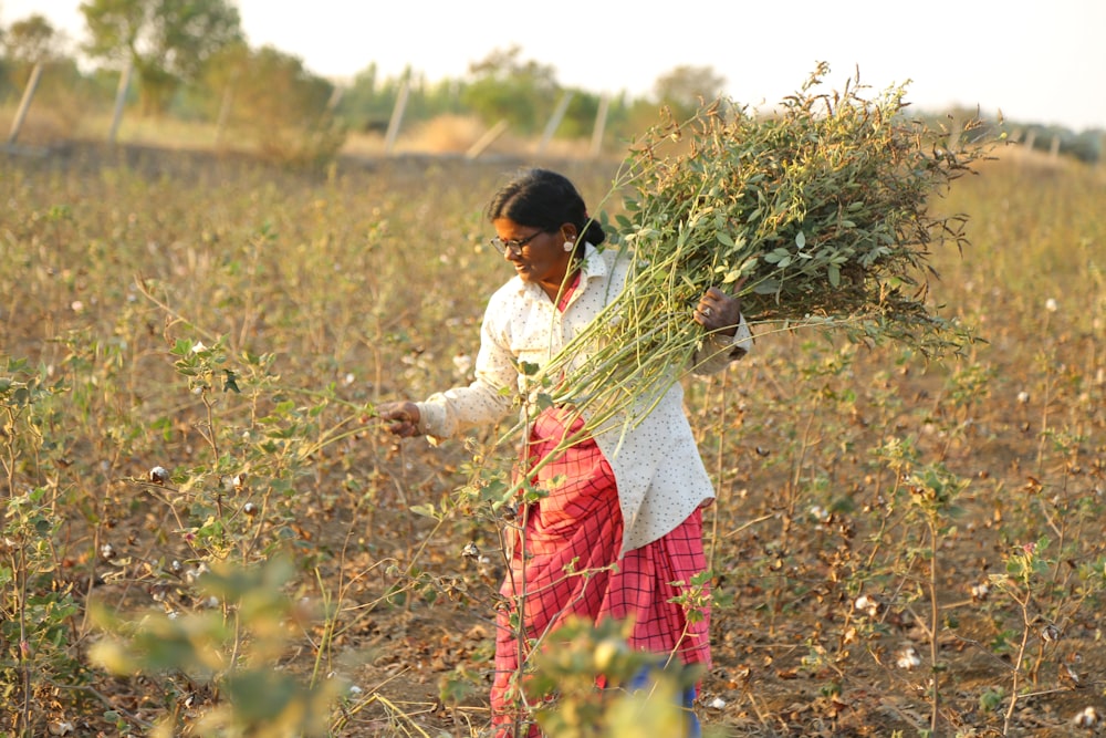 a woman standing in a field holding a bundle of plants