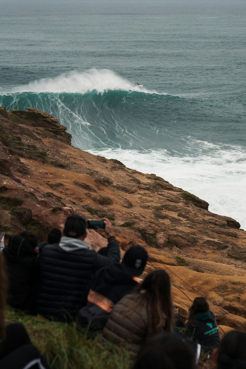 a group of people sitting on a cliff watching a wave