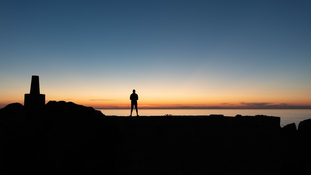 a silhouette of a person standing on top of a cliff