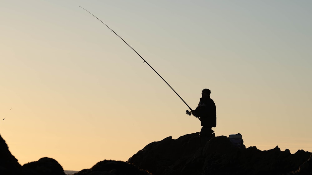 un uomo in piedi sulla cima di una roccia mentre tiene una canna da pesca
