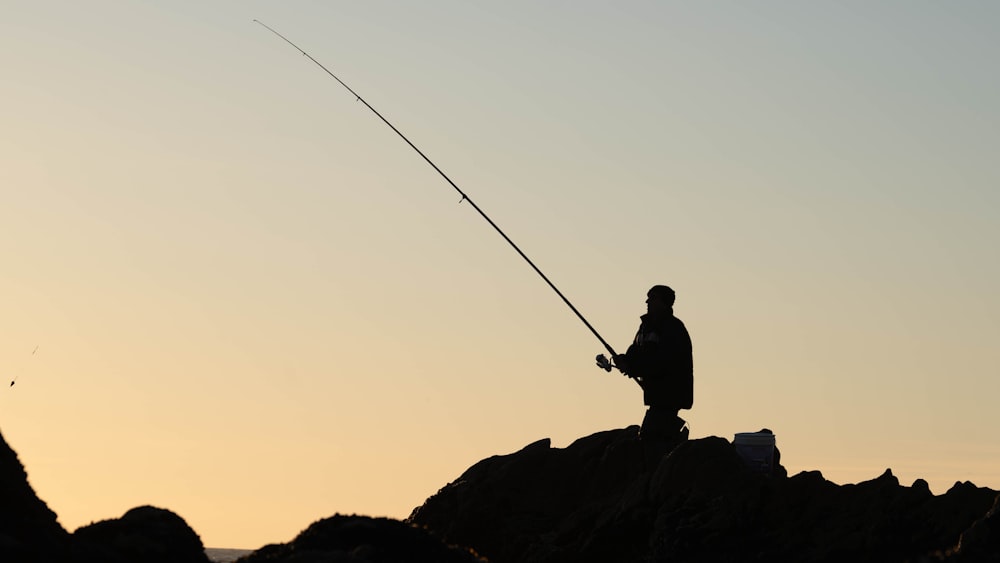 a man standing on top of a rock while holding a fishing pole