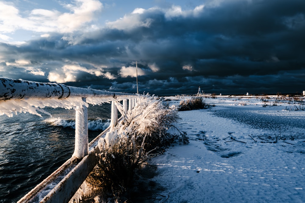 a snow covered beach next to the ocean under a cloudy sky