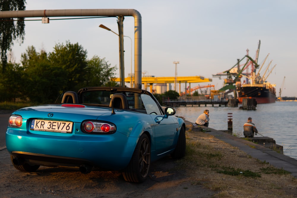 a blue sports car parked next to a body of water