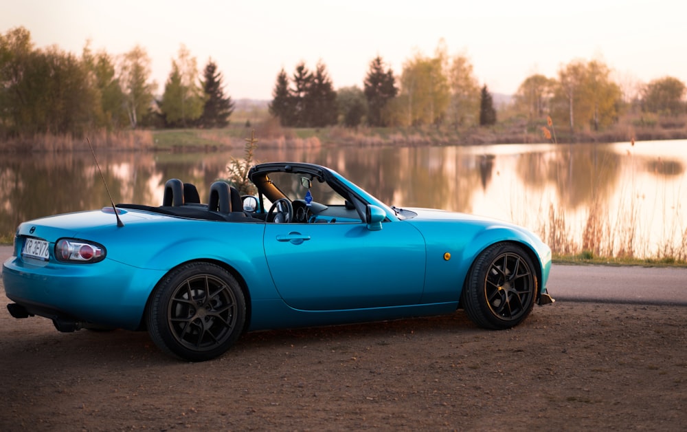 a blue sports car parked next to a lake