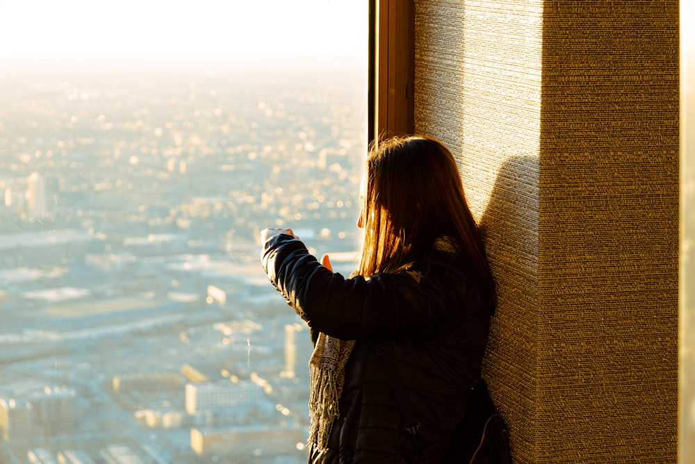 a woman standing next to a window looking out at a city