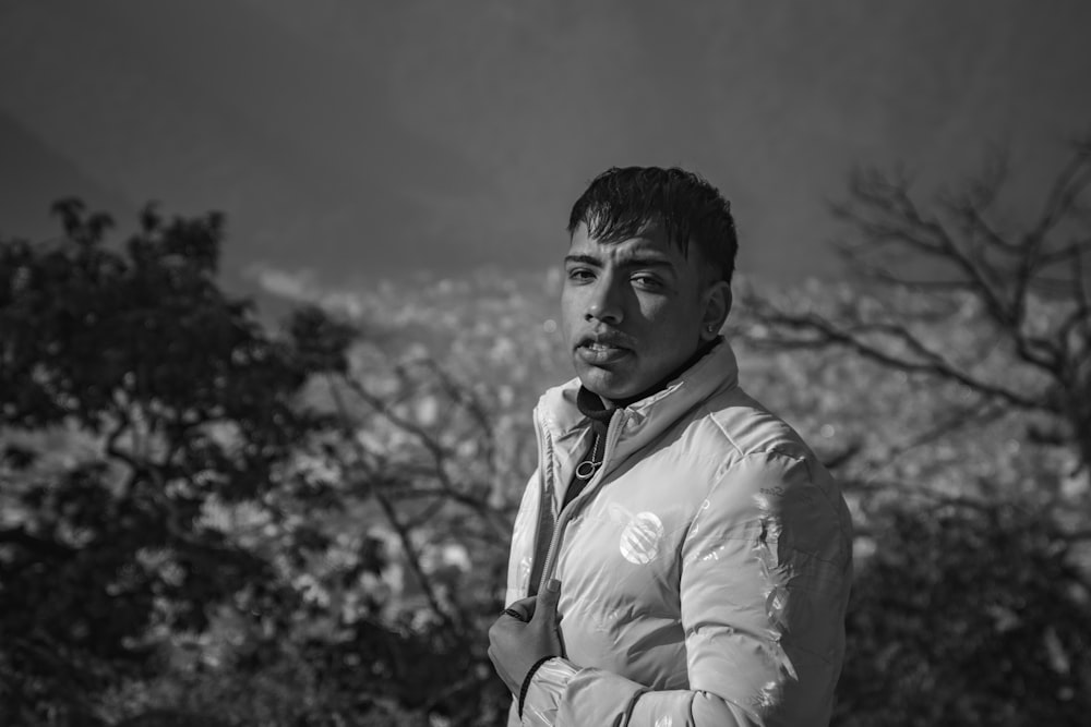 a man in a jacket and tie standing in front of trees