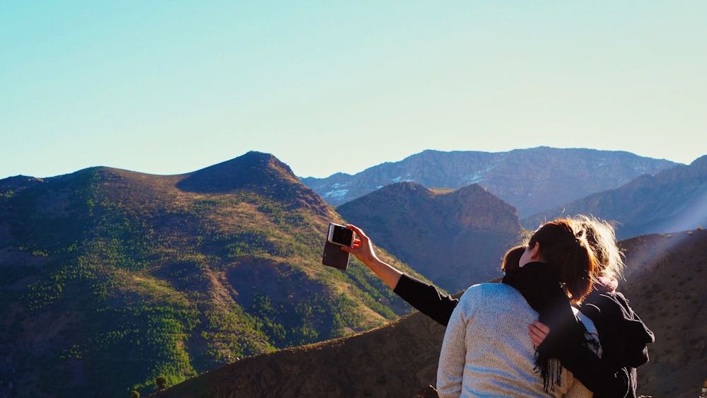 a woman taking a picture of the mountains with her cell phone