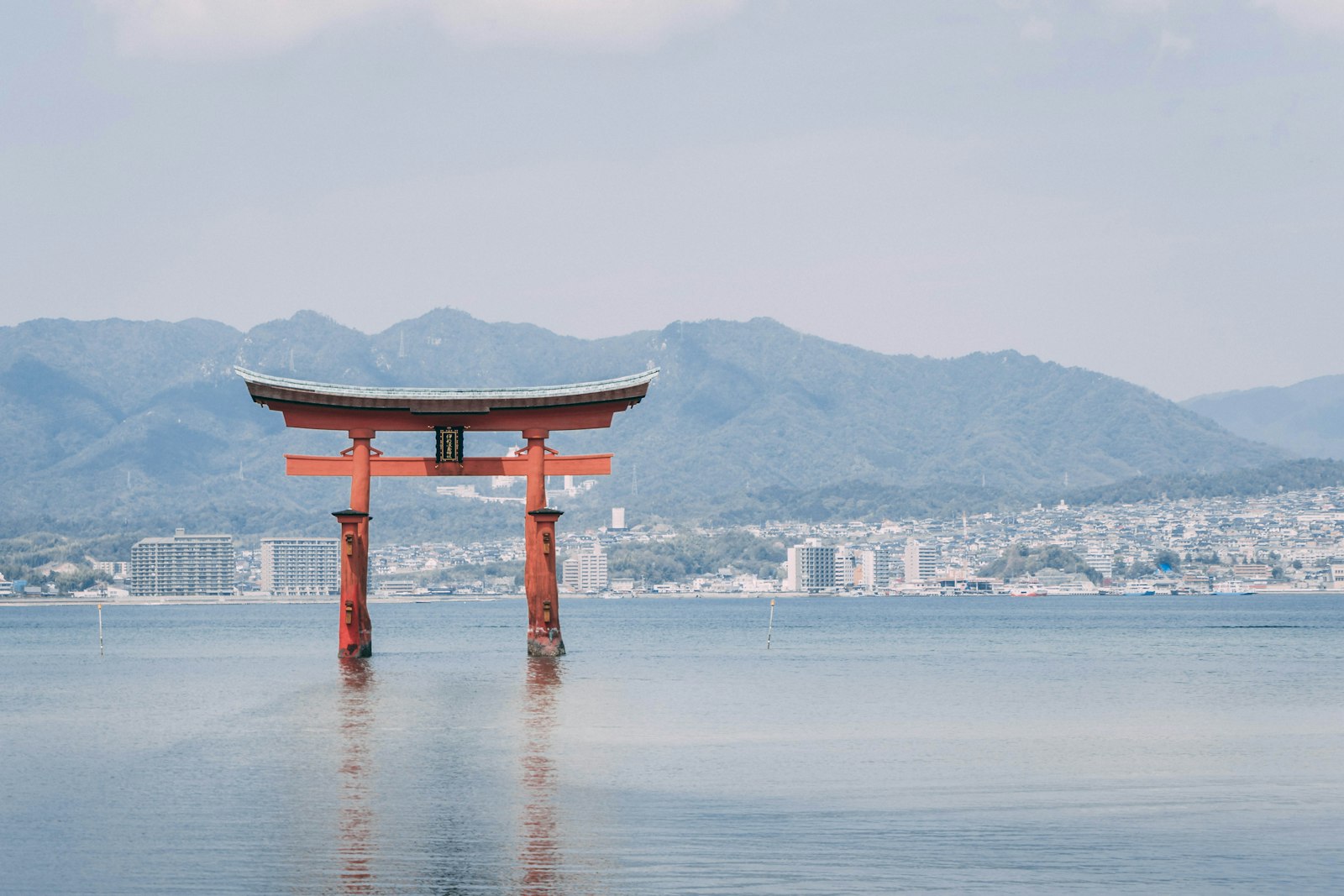 The great vermilion torii of Itsukushima Shrine standing in the water off Miyajima, with mountains behind