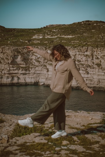 a woman standing on top of a rock near a body of water