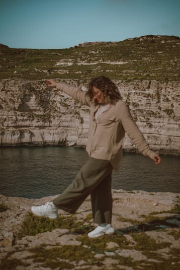 a woman standing on top of a rock near a body of water