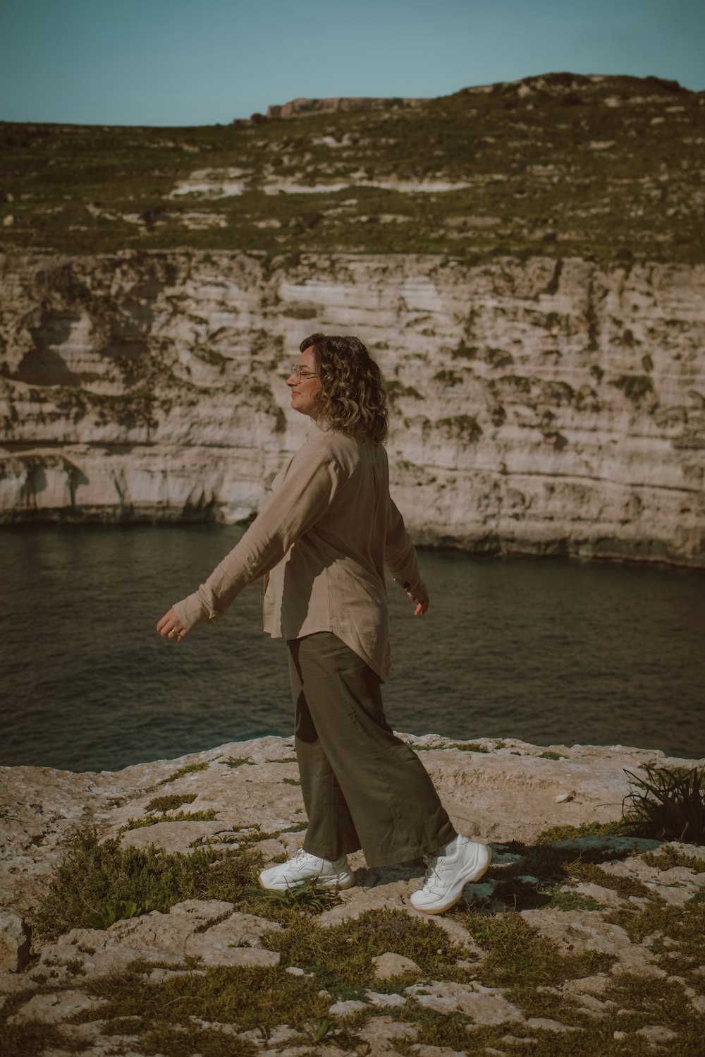 a woman standing on top of a cliff next to a body of water