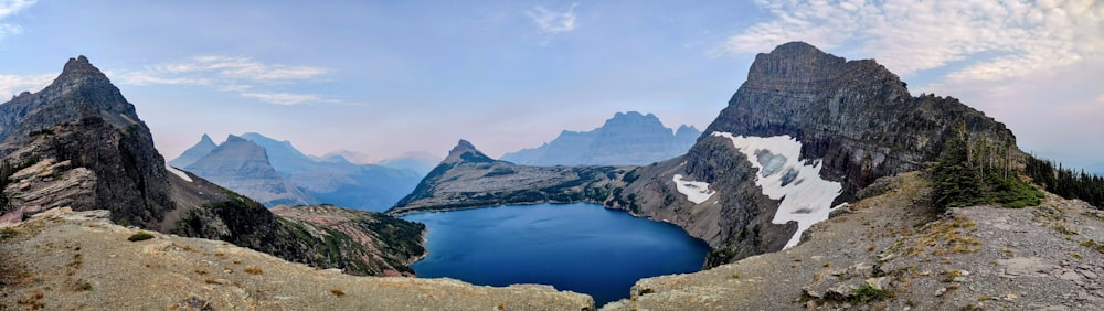 a lake surrounded by mountains under a cloudy blue sky