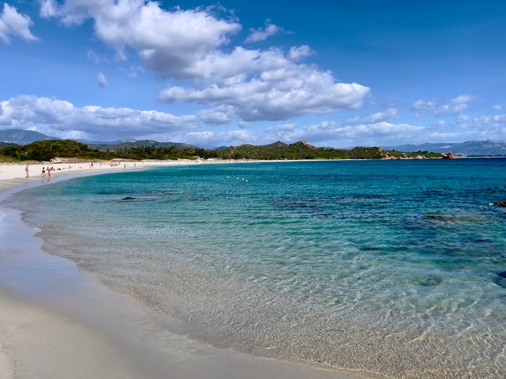 a sandy beach with clear blue water under a cloudy blue sky