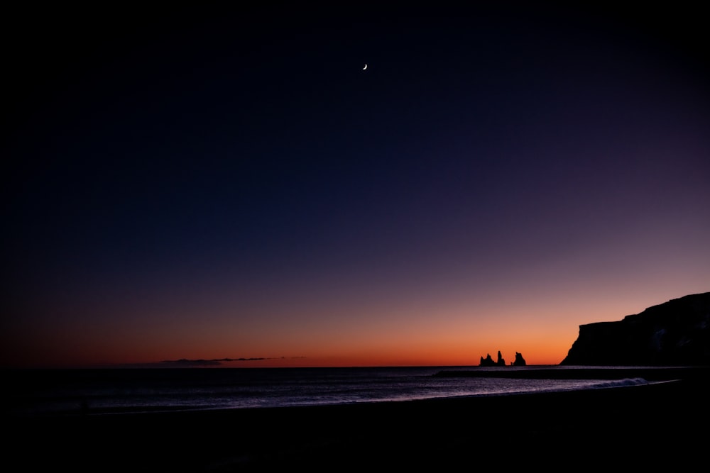 the sun is setting over the ocean with a rock outcropping