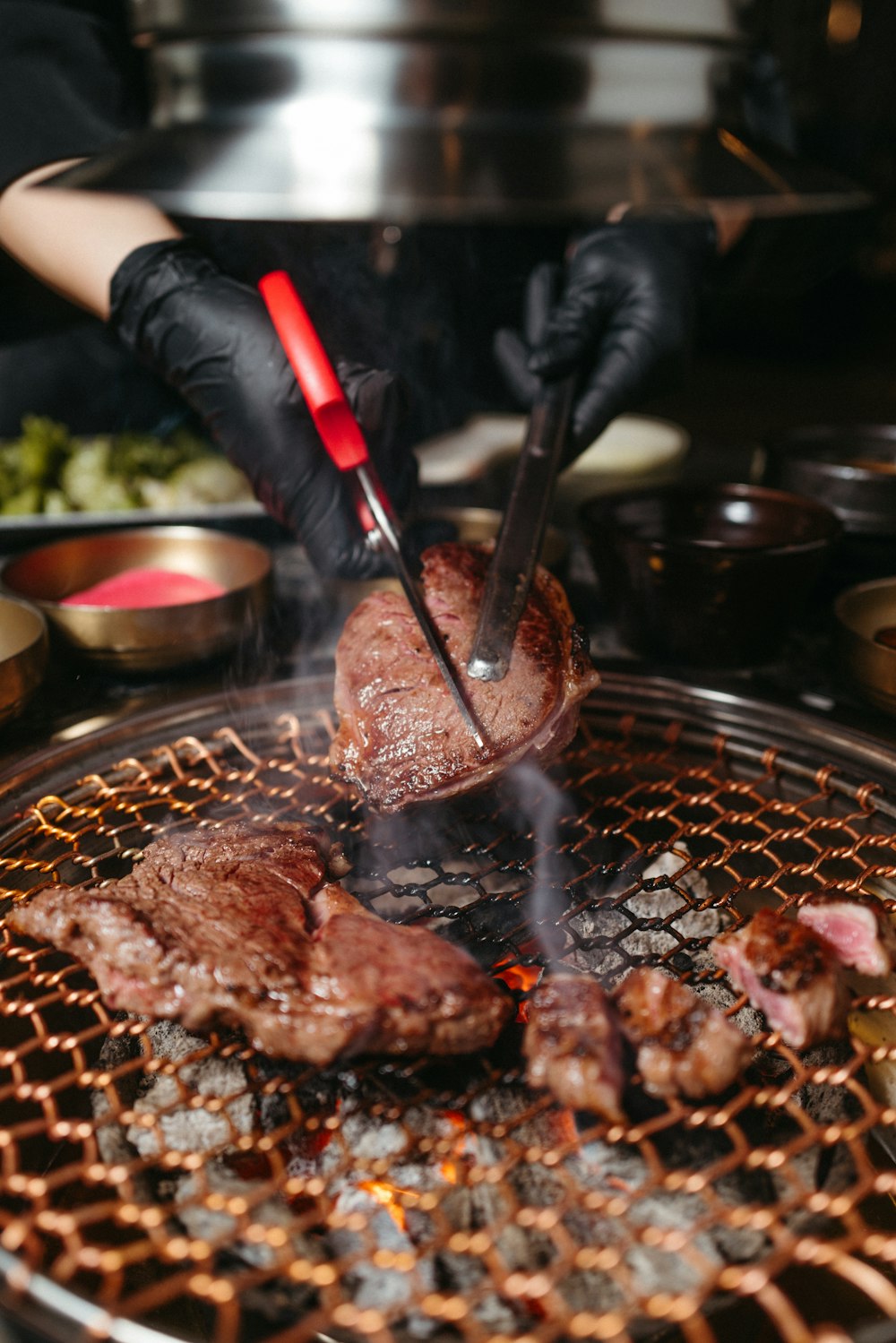 a person cooking steaks on a grill with tongs