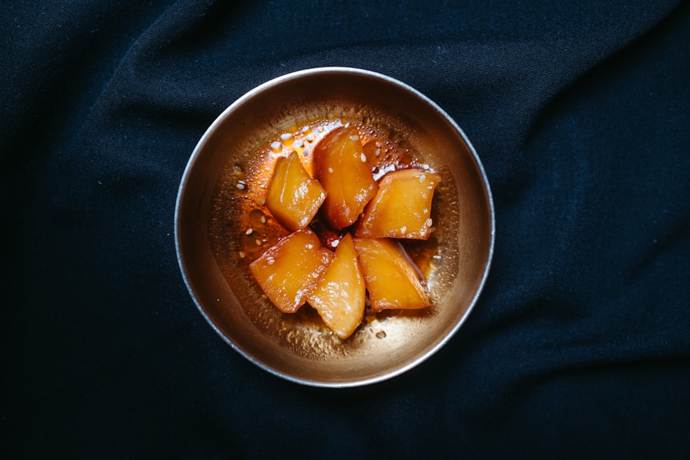 a metal bowl filled with fruit on top of a black cloth